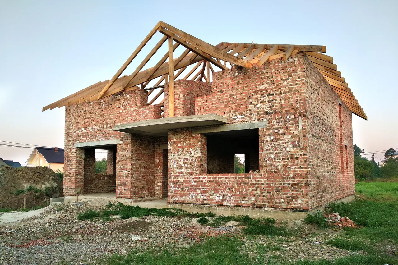 Murowany dom w trakcie budowy na porośniętej trawą działce